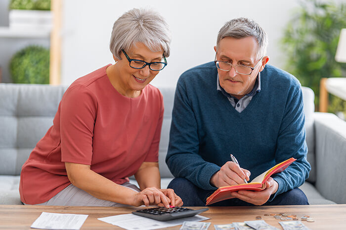 Ein älteres Ehepaar sitzt am Schreibtisch und berechnet die Kosten der Betreuung, um das Familienbudget zu verwalten.