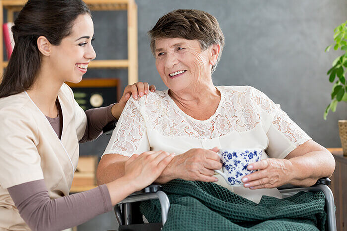 Betreuerin im Gespräch mit einer Rentnerin im Rollstuhl bei einem Tee.